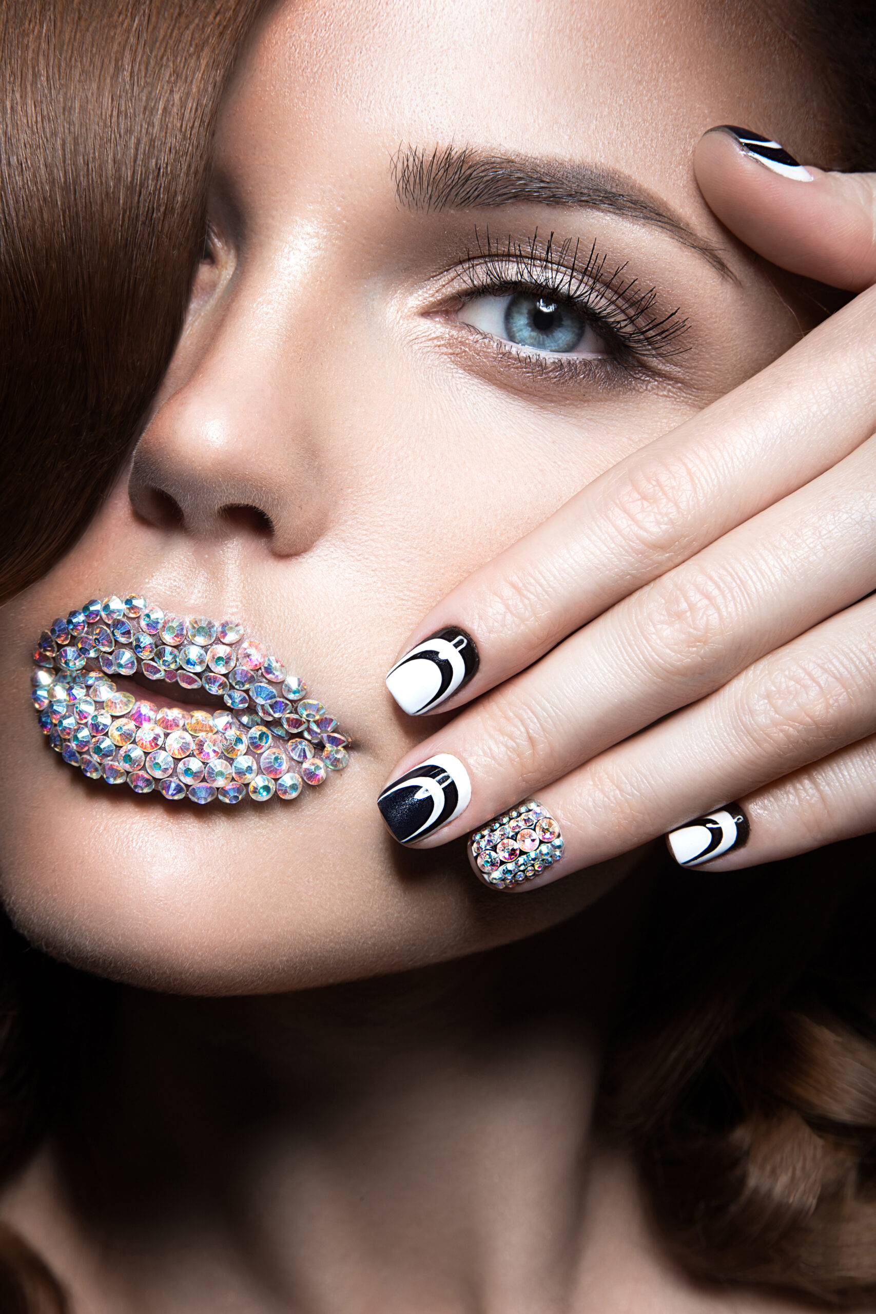 Beautiful girl with bright nails and lips of crystals, long eyelashes and curls. Beauty face. Picture taken in a studio.