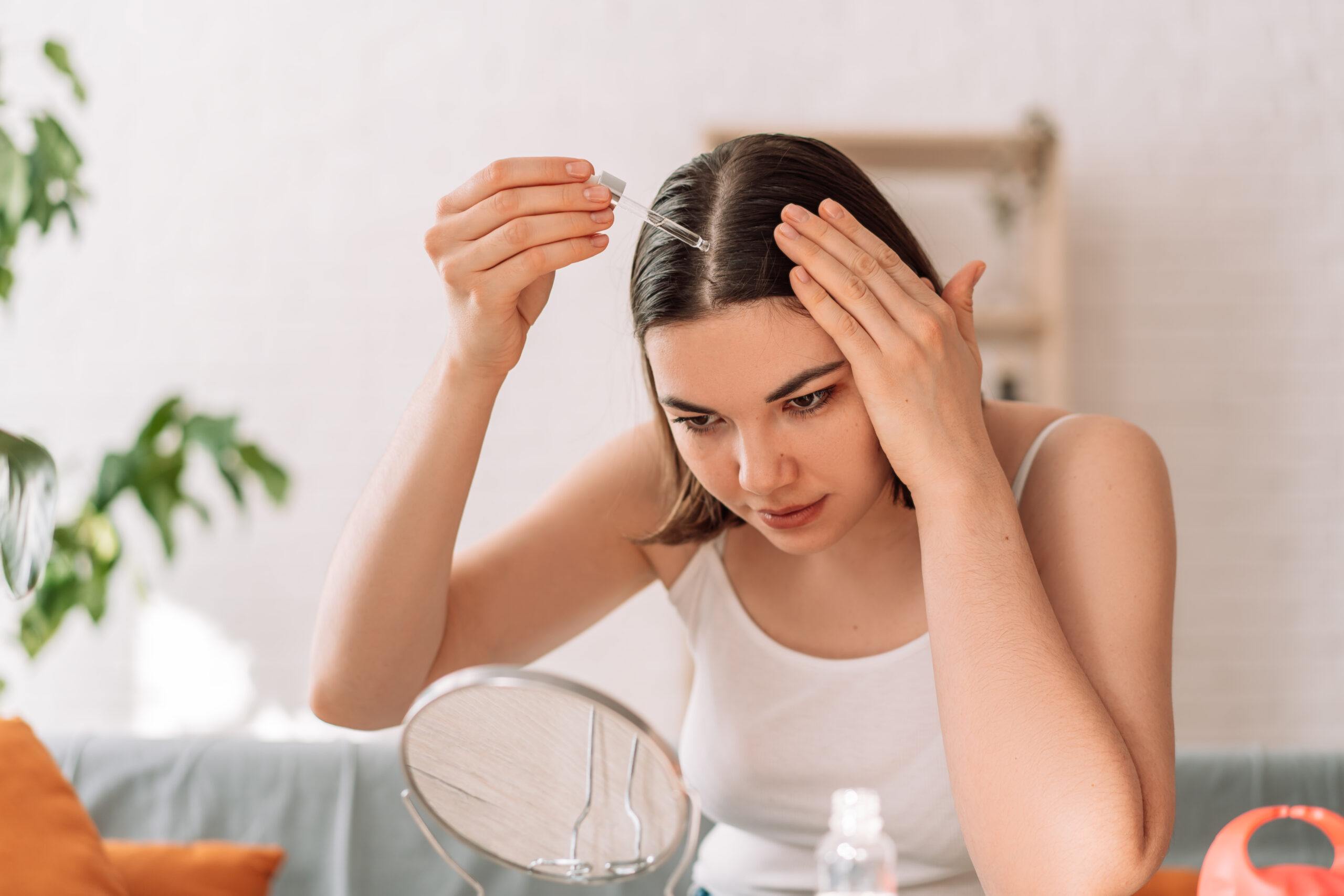 A woman is doing haircare for her hair by applying natural oil to her scalp.