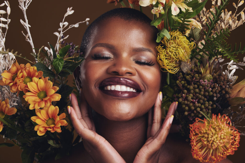 Skincare, cosmetics and protea with the face of a black woman in studio on brown background for nat.