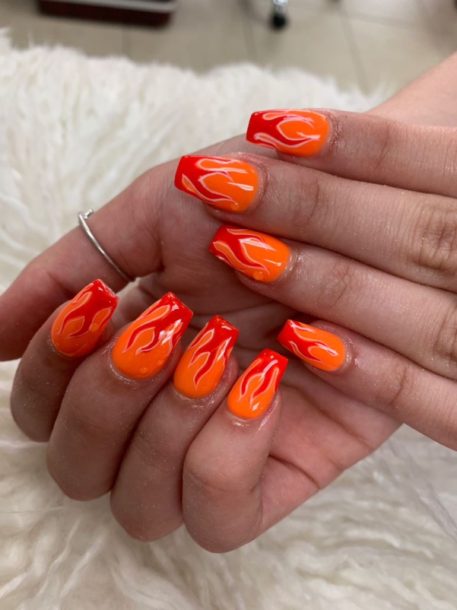 A woman's hands adorned with a fiery orange manicure for Fall 2023; showcasing the trendiest nail colors of the fall season. Fall 2023 Nail Colors