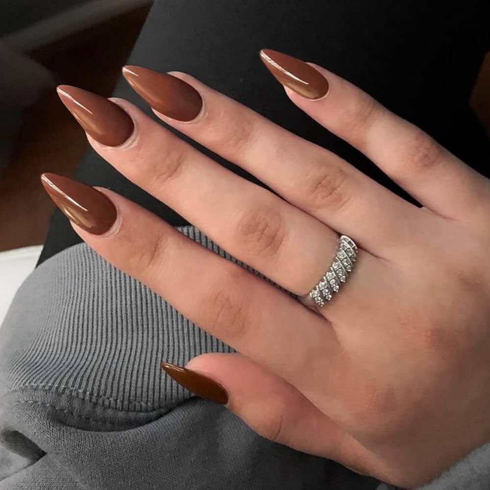 A woman's hand showcasing brown nails adorned with a diamond ring.