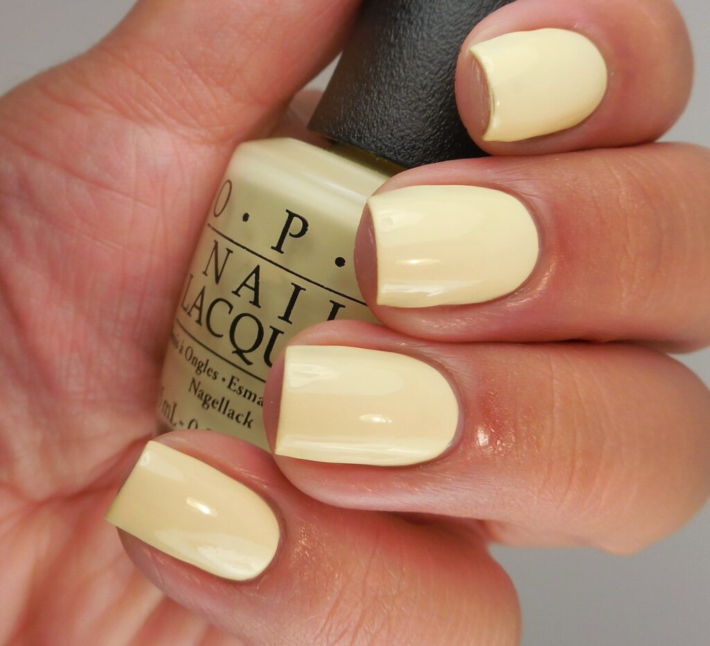 A woman's hand holding a nail polish shade from OPI in the yellow soft pastel tone