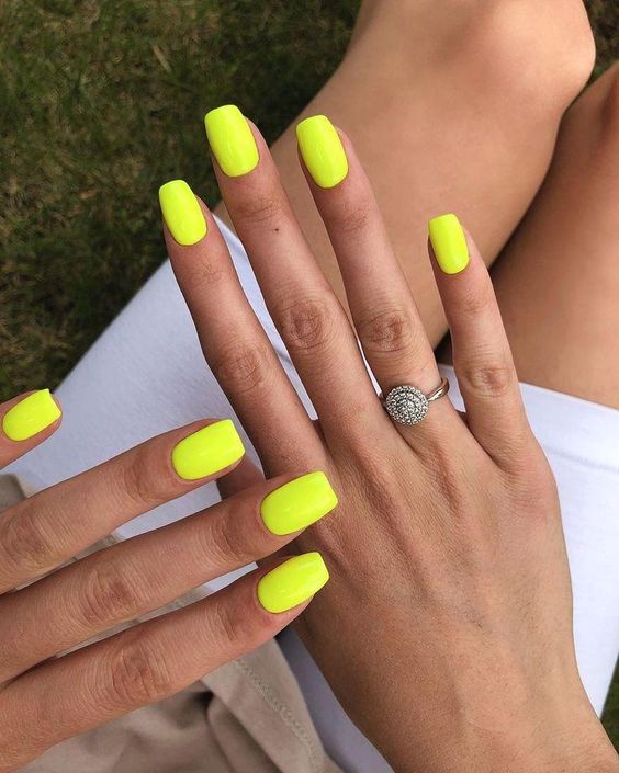 A woman wearing a white skirt and a  vibrant lemon summer yellow nail polish shade