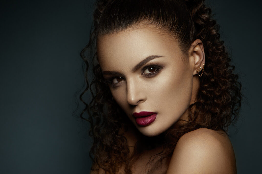 Beautiful face of a fashion model with black eyes.Curly hair. Pink lips. Studio portrait. Makeup products