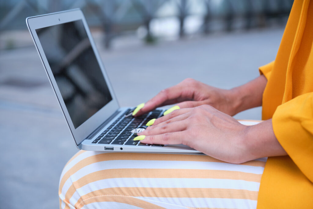 Unrecognizable businesswoman wearing yellow suit jacket working with a laptop sitting outdoor.