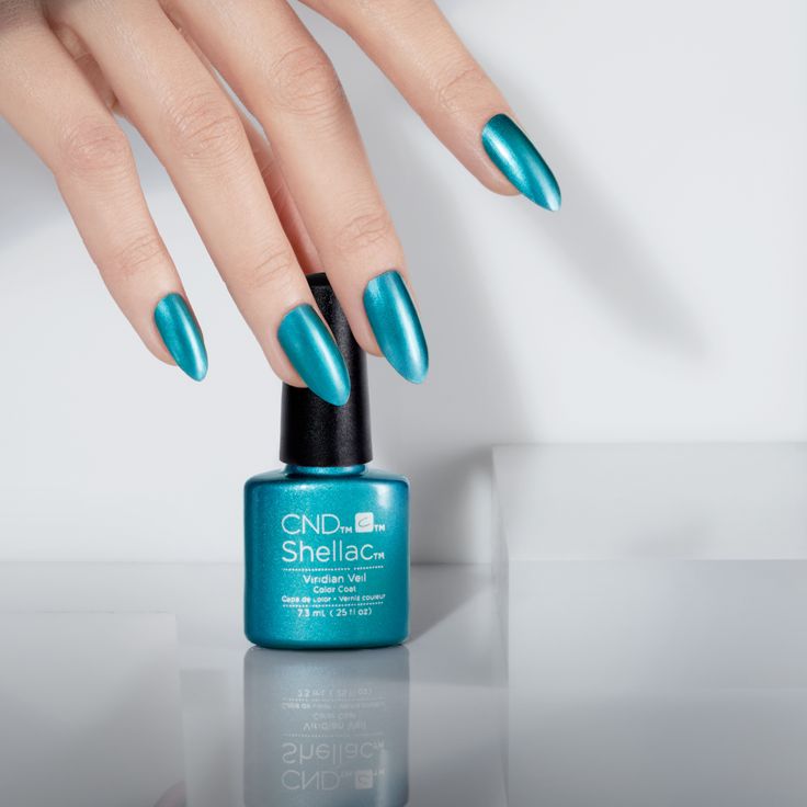 A faceless woman with blue-painted nails from CND Shellac is holding a glossy blue nail polish bottle on a white background.