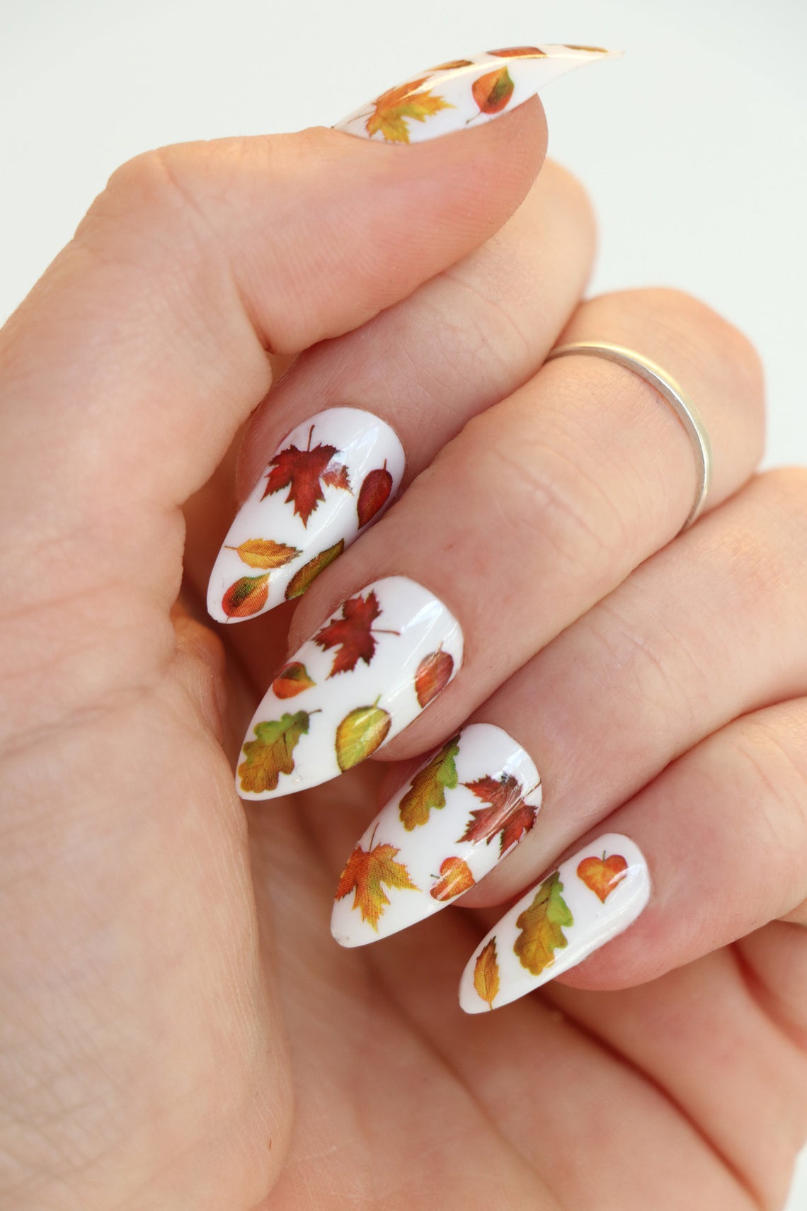 A woman's nails elegantly showcase an autumn-inspired manicure, beautifully crafted in the shape of fallen leaves.