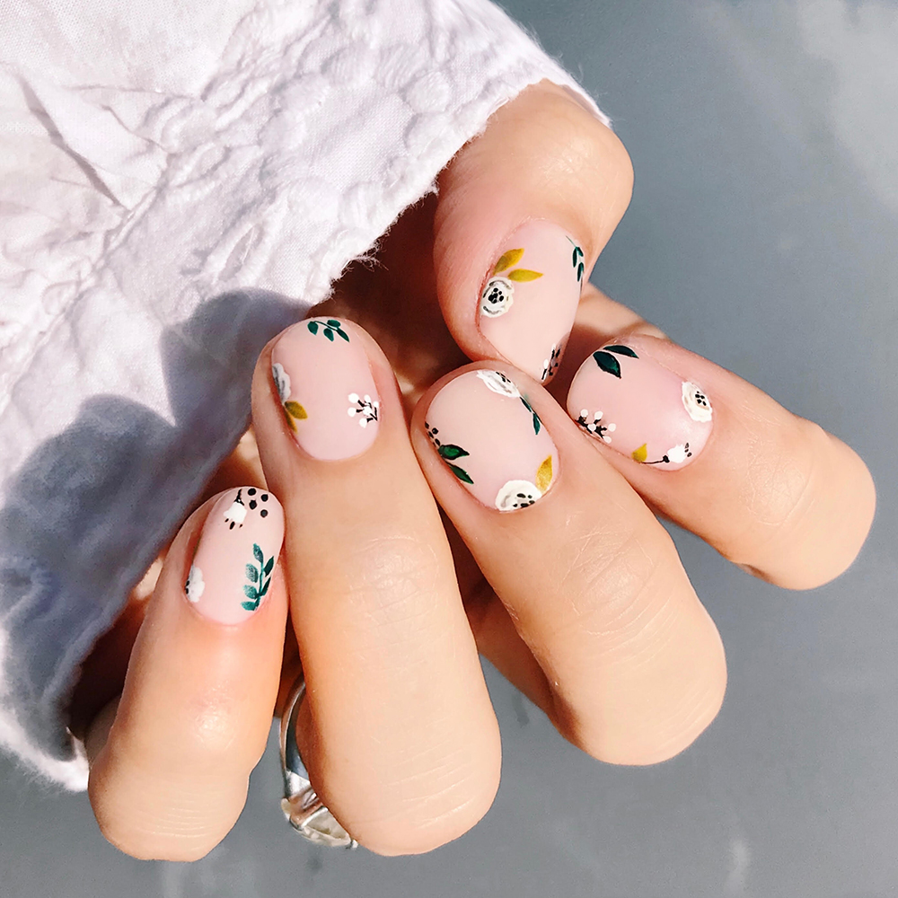 A woman's nails with autumn designs, leaves, flowers, and black points on the light pink nail shade base