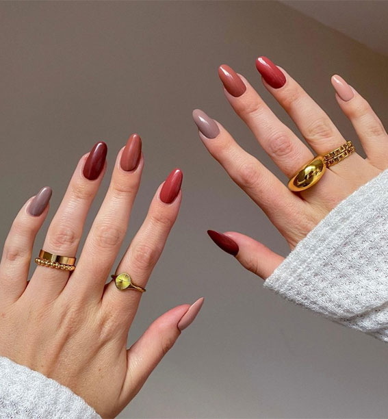 A woman's hands are wearing gold rings on her fingers, and her nails are painted with fall nail shades that suit the nail trend