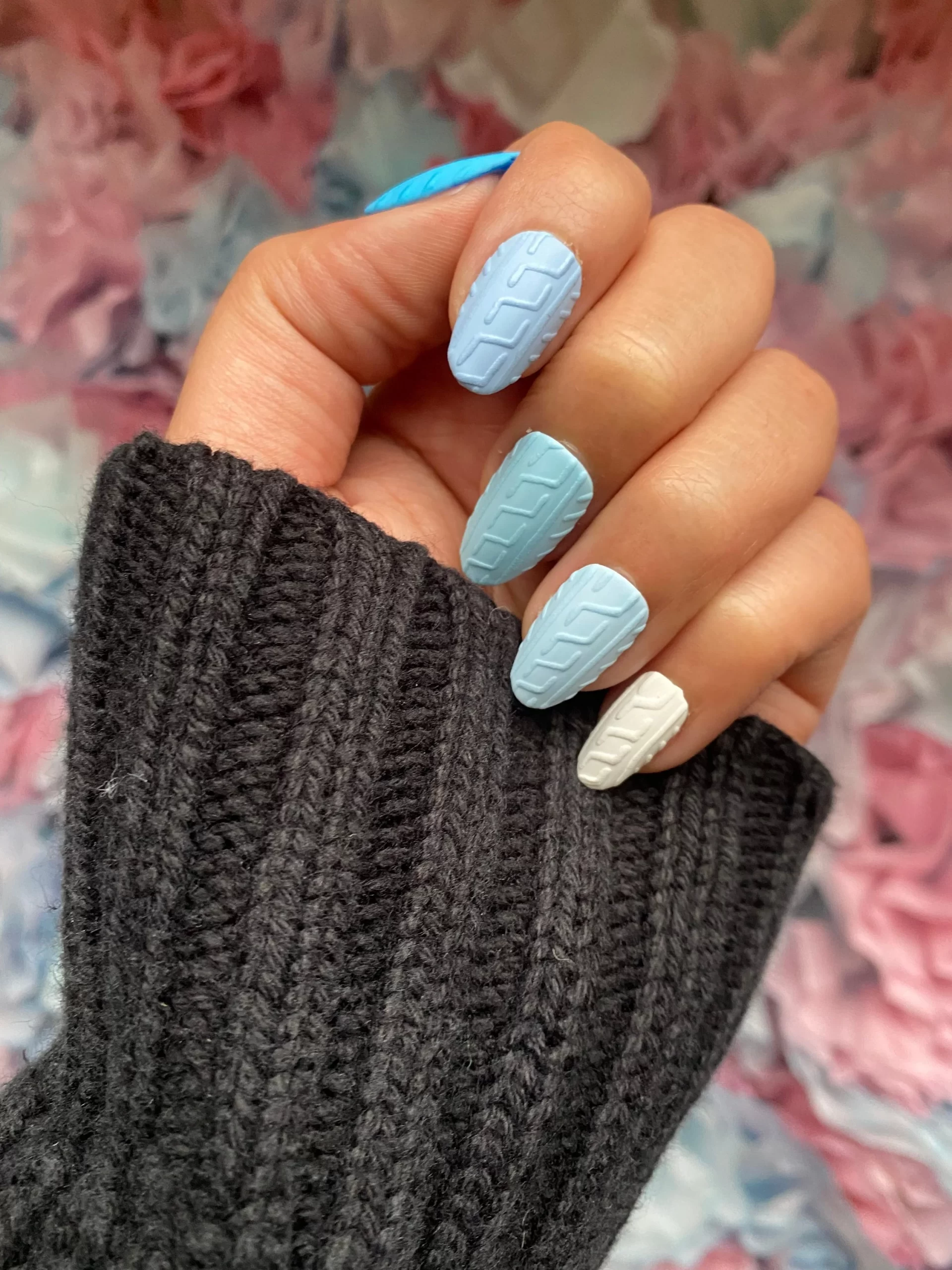 Wearing a bold gray fall sweater, she matches it with a light blue nail design shaped like a cozy sweater, embracing the essence of the season.