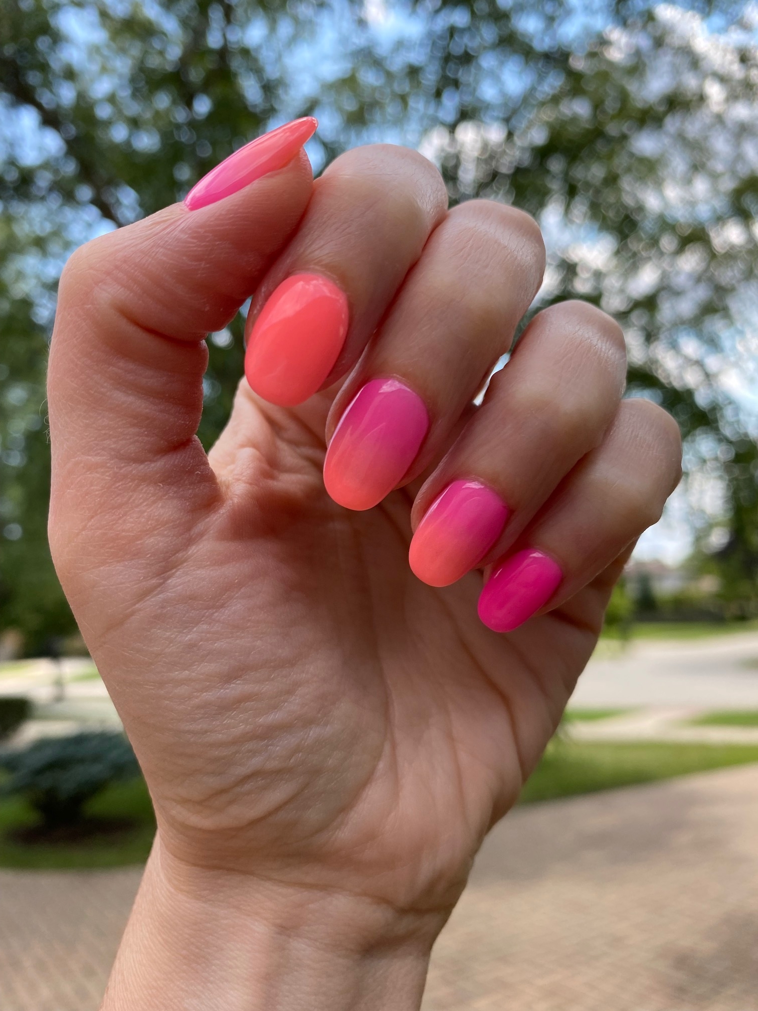 A woman's hand showcases sunset pink nails within a manicure blending shades of pink and orange.