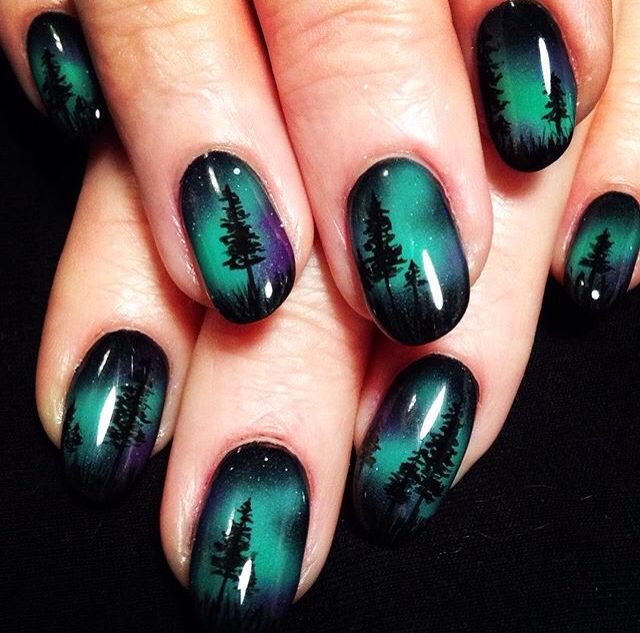 A woman's nails are painted with trees and the aurora borealis for Halloween Nail Art.