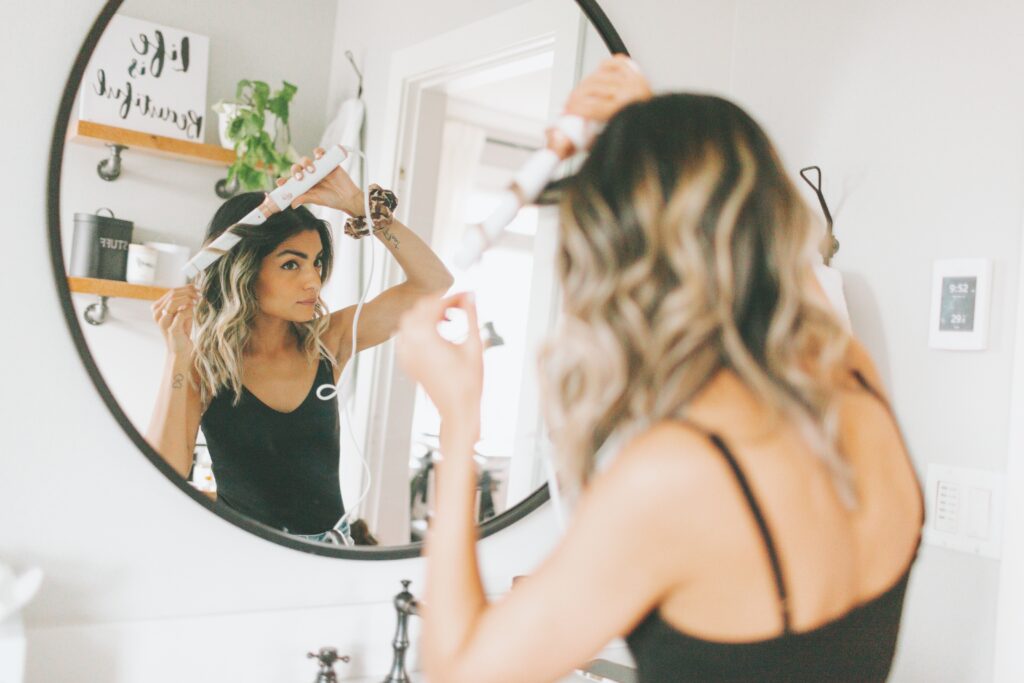 a-woman-curling-her-hair-in-the-bathroom-mirror-2022-11-15