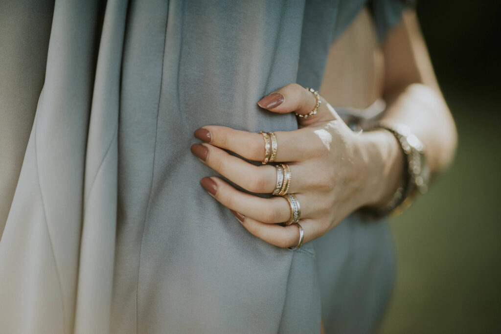 A closeup of a female with brown nail polish and rings standing outdoors with crossed arms