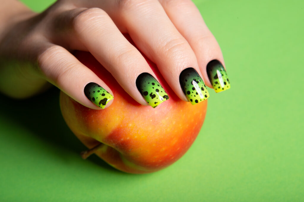 Female neat hand with short natural nails painted with green nail polish holding apple. Natural, cozy, elegant, modern look. 