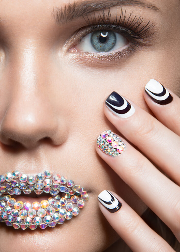 Beautiful girl with bright nails and lips of crystals, long eyelashes and curls. Beauty face. Picture taken in a studio.