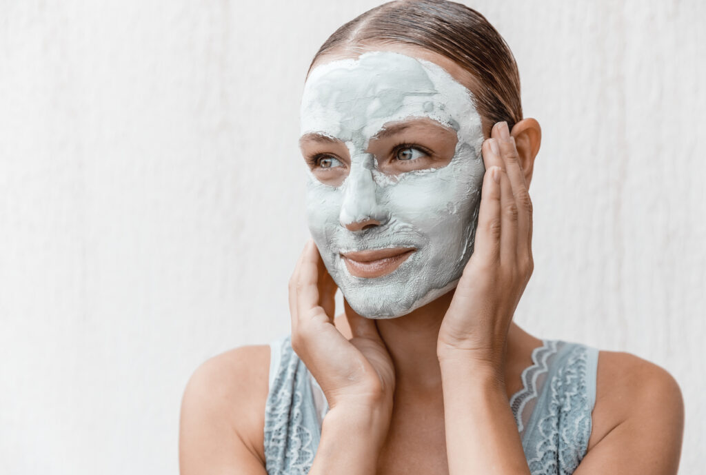 Closeup Portrait of a Pretty Girl with Cream Mask on her Face Isolated on White Background. Using Clay for Perfect Skin. Beauty Treatment Concept.