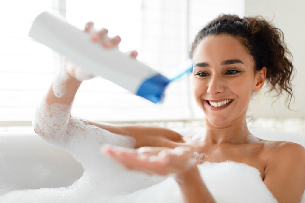 Beautiful young woman lying in a warm bath, using shampoo or foam at home. Lovely millennial lady enjoying a domestic spa procedure, relaxing in a bathtub.