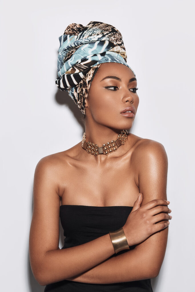 Effortless beauty. Attractive young African woman in turban looking away and keeping arms crossed while standing against grey background