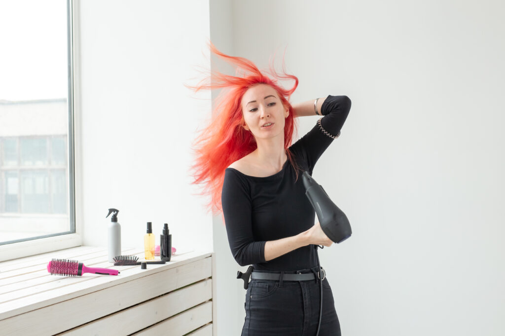 Hairdresser, beauty salon and people concept - young woman hair stylist with hair dryer on white background. hair tools