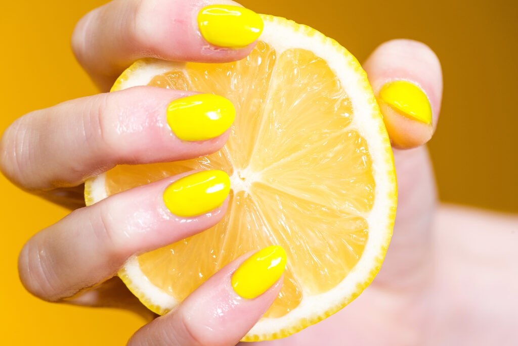 Hand holds yellow lemon in front of lemon background, Summer Nail Trends