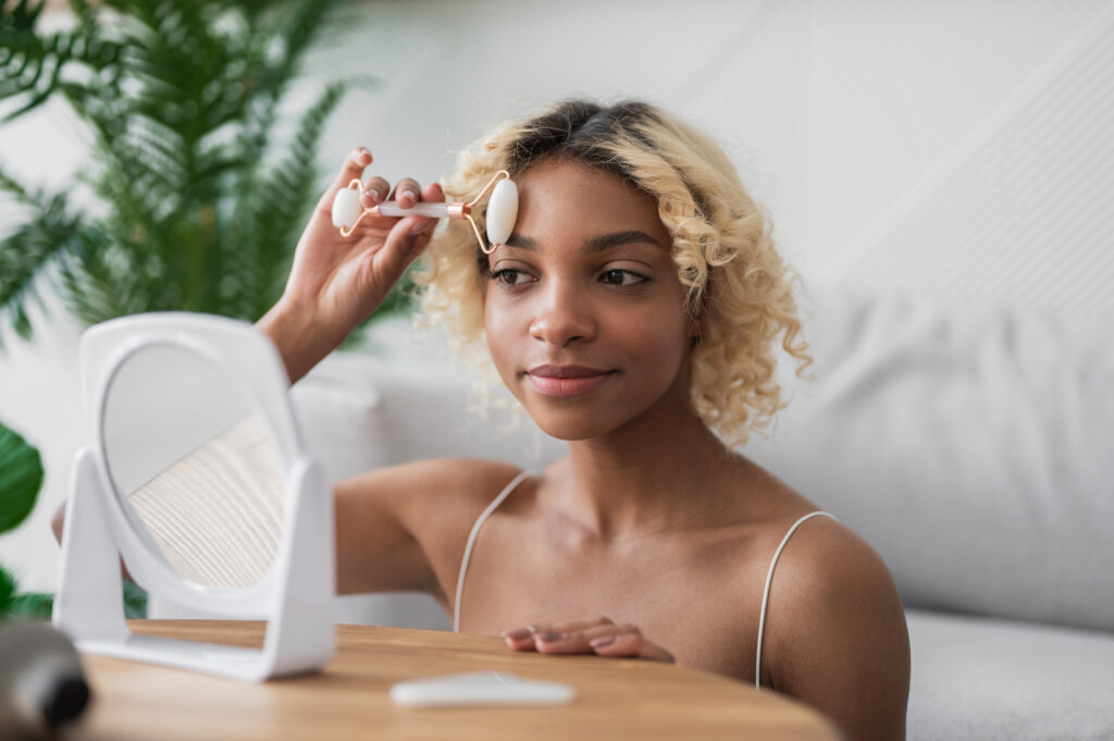 Morning beauty routine. Smiling woman massaging face with y-shaped jade roller at home.