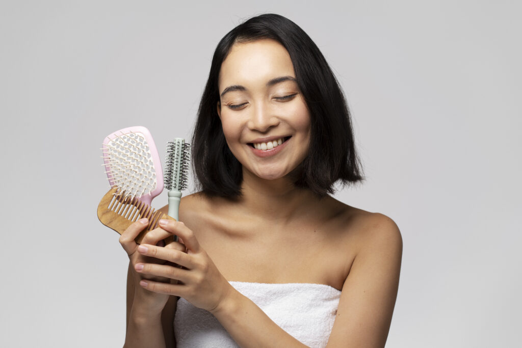 Hair care and beauty concept. Portrait of positive brunette woman holding hair brushes and posing isolated over white studio background. Hair treatment concept