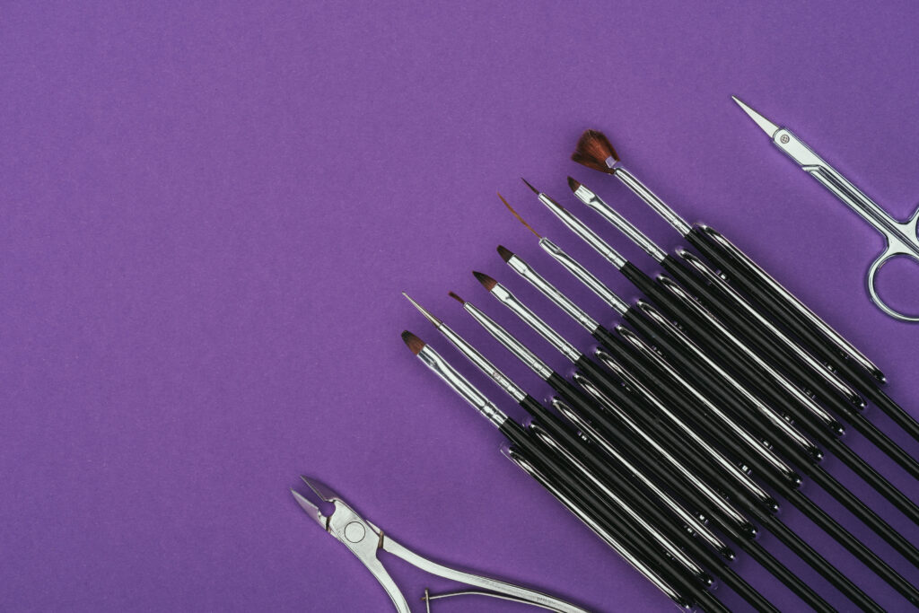 top view of brushes, scissors and nail nippers isolated on purple