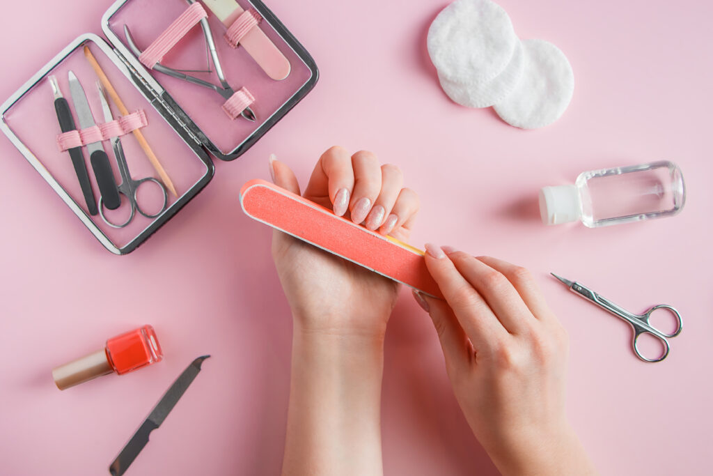 Woman does a manicure at home. Hands with a nail file on a pink background. Ombre nails. Home nail care.