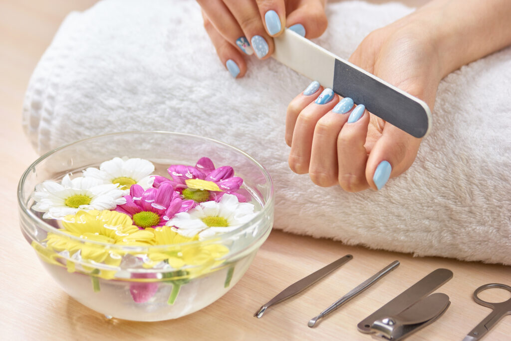 Woman filling nails on towel. Young woman hands in spa salon polishing manicured nails, bath for hands, manicure equipment. coffin nails