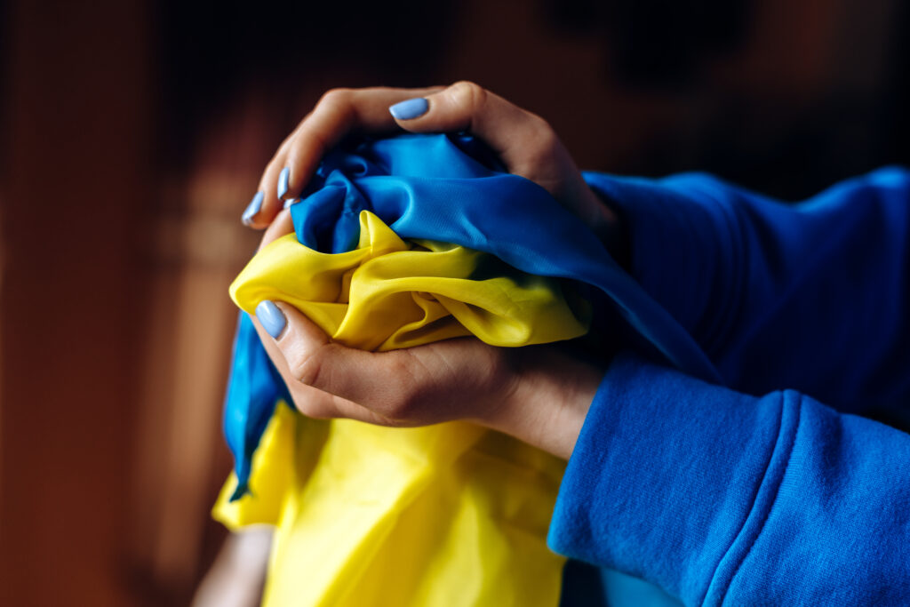 The yellow-blue flag of Ukraine is at the hands of the woman with nails painted at the blue and yellow colours. Martial law in Ukraine 2022. Stop war and peace concept