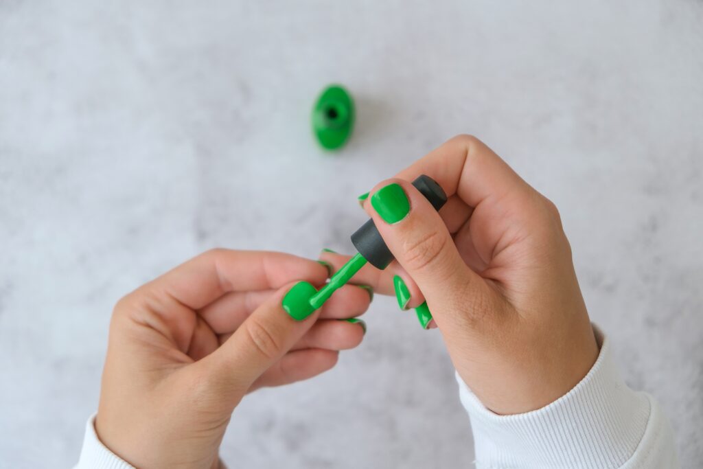 Manicured female hands with stylish green nails holding bottle of nail polish. Trendy modern design manicure. Gel nails. Skin care. Beauty treatment. Nail care. Wellness. Trendy colors.