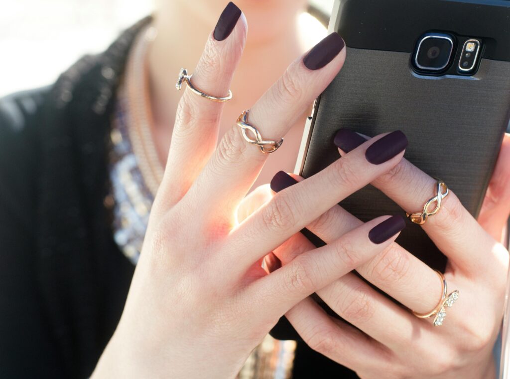 A faceless woman holding a mobile phone, her nails painted with bold purple nail polish shade