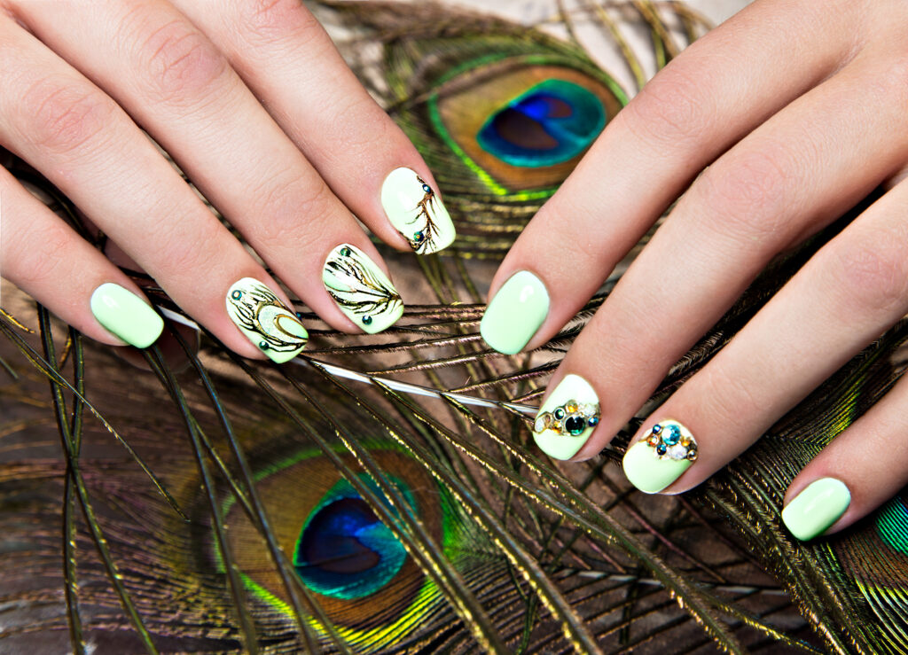 Art design manicure with peacock feather on female hands. Close-up. Fashion nails. Spring nail polish colors