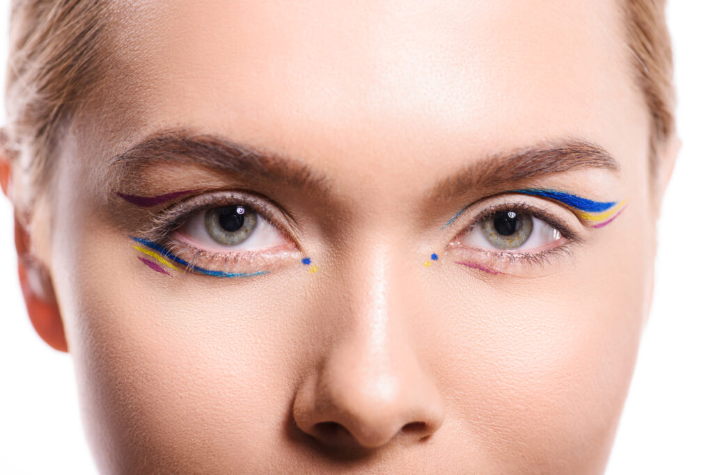 woman with colored makeup with lines looking at camera isolated on white. apply colorful eyeliner