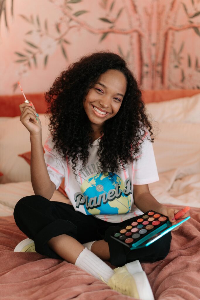 A beautiful girl with curly black hair holding a colorful eyeshadow palette