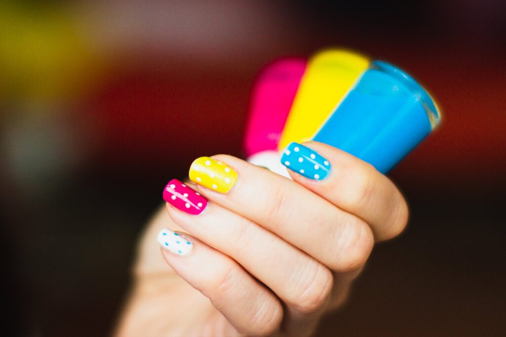 A woman is holding colorful papers with colorful painted nails with white dots.