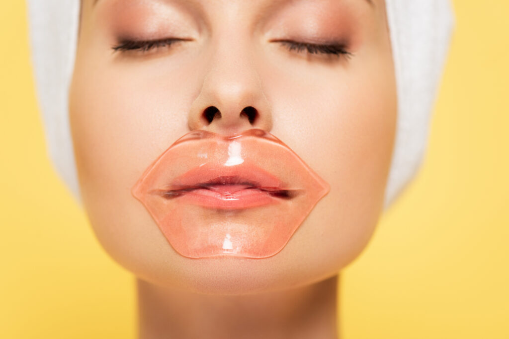 close up view of beautiful woman with lip patch and closed eyes isolated on yellow. Lip mask