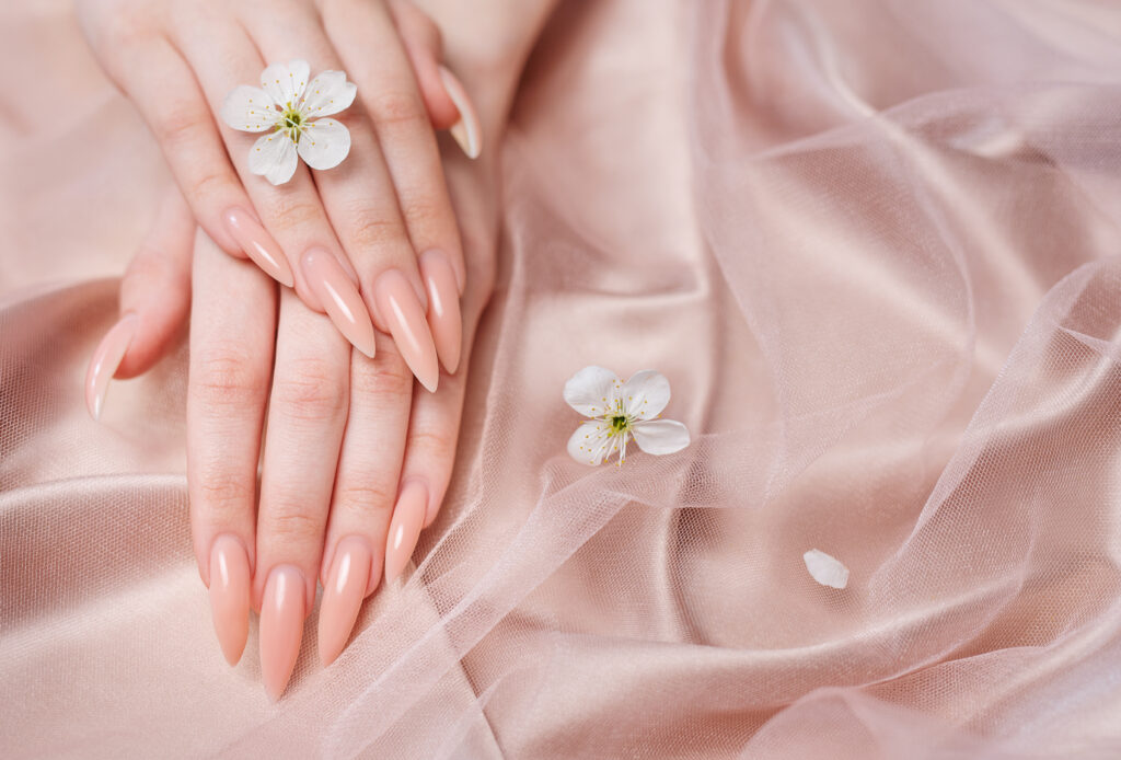 Elegant pastel pink natural manicure. Female hands  with Cherry blossom flowers  on pink silk background.