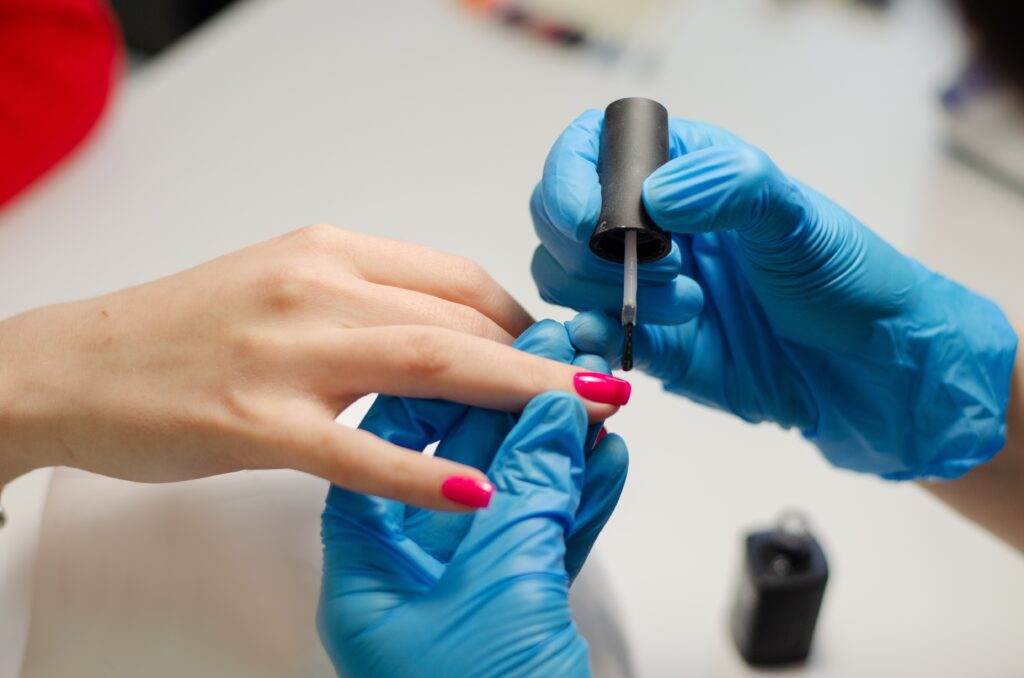 Pretty young female nails in doing her nails using brush to apply gel polish