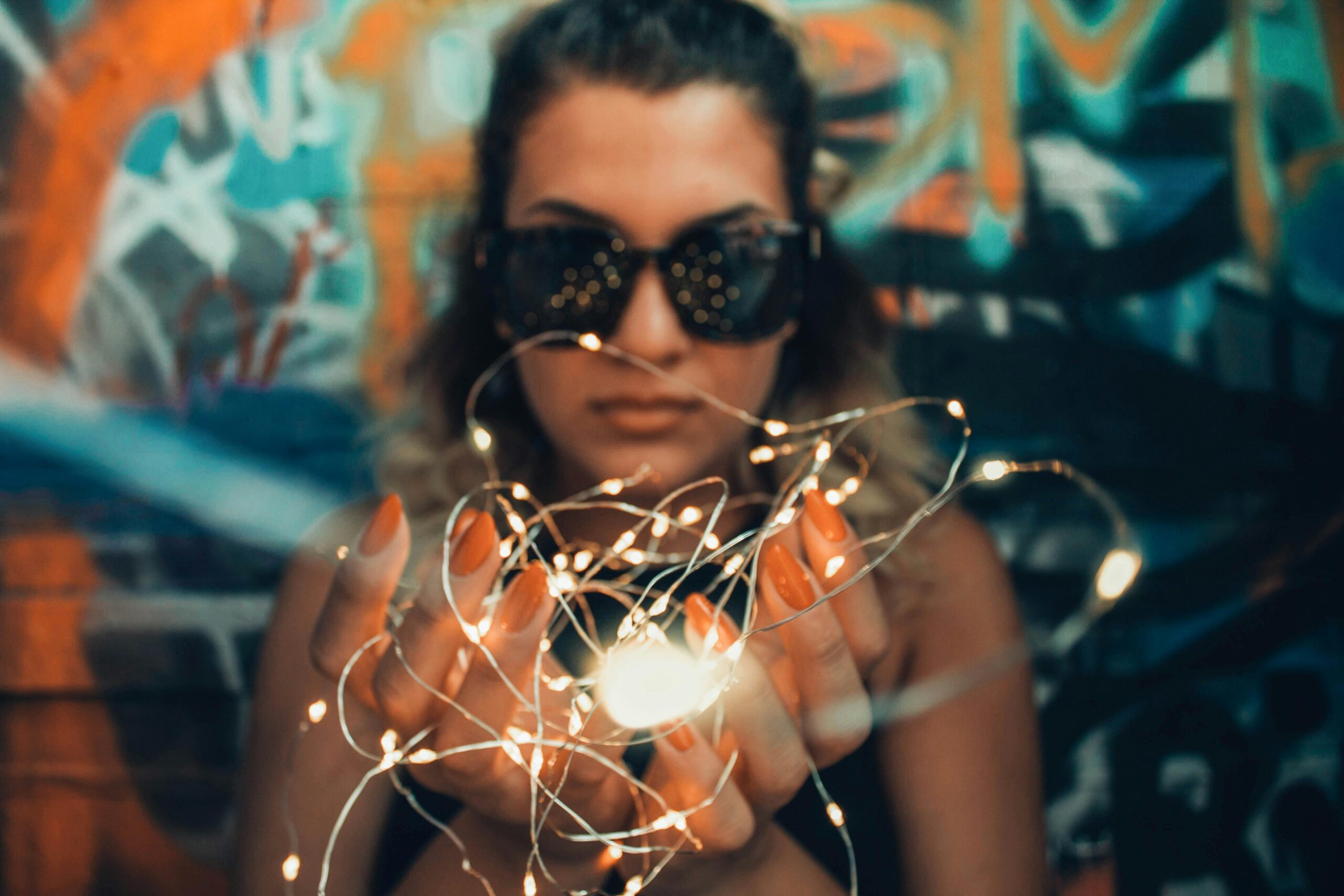 a woman wearing sun glasses, her nails painted in orange, 2024 nail trends