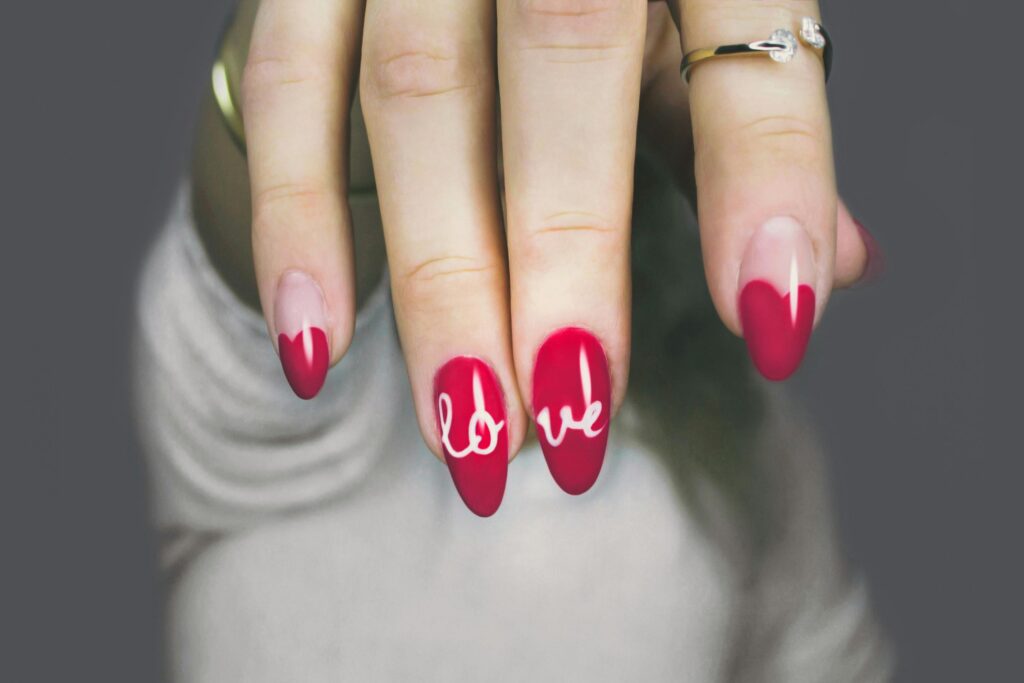 A faceless woman nails painted in red with the word " Love " in white as a nail design