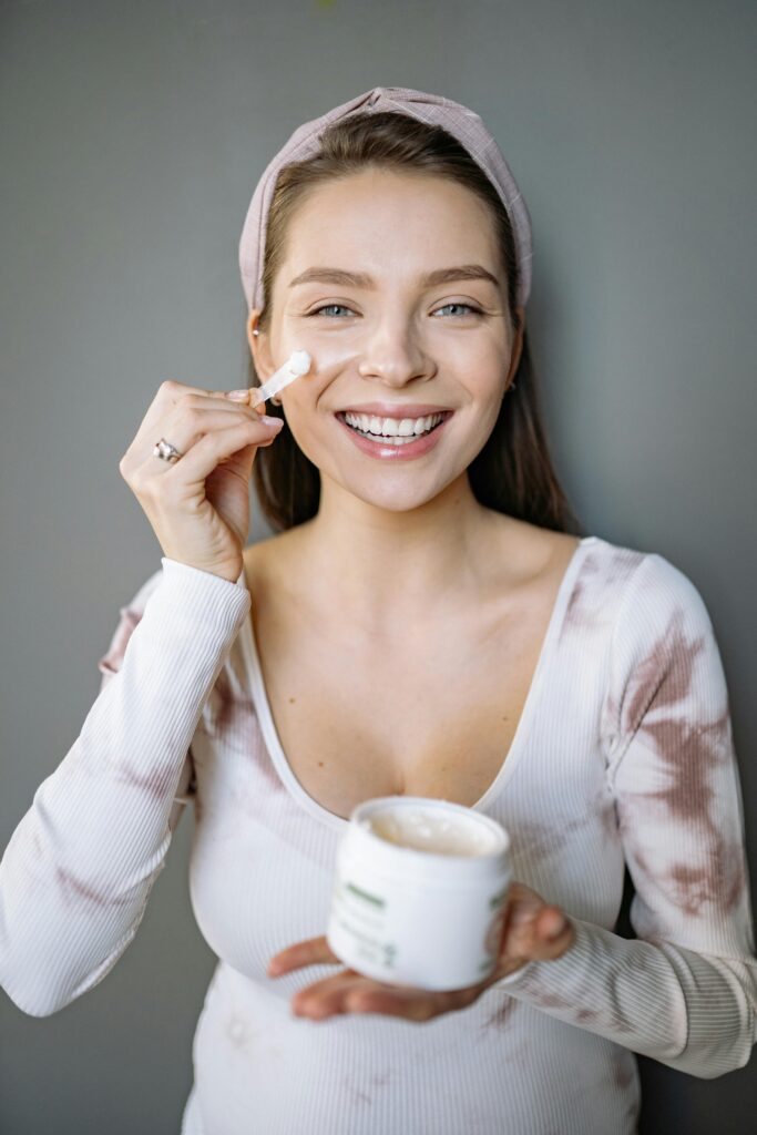 A beautiful smiling woman is doing her morning skincare and applying a facial cream.