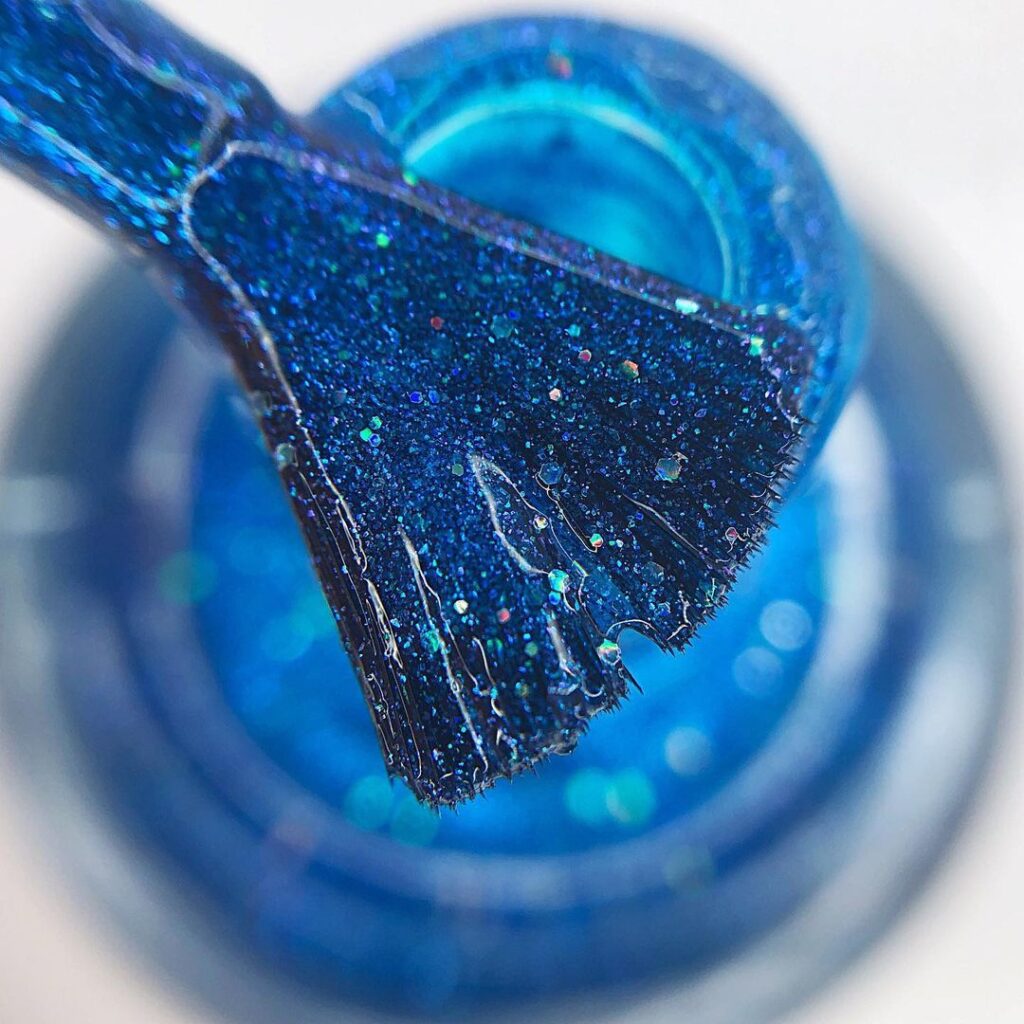 A glitter nail polish bottle sits alongside its shimmering brush, both infused with the enchanting shade.