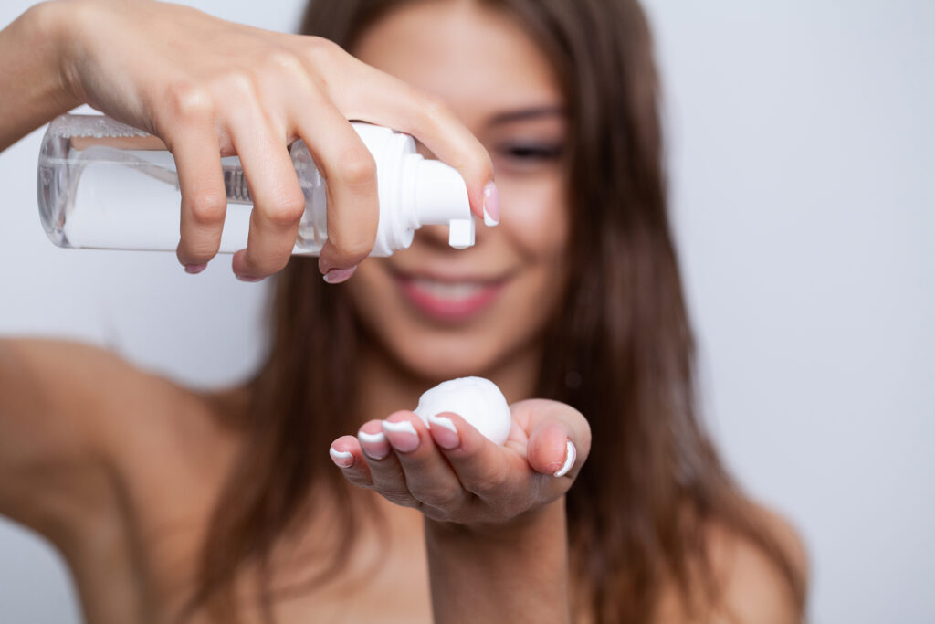 Beautiful young woman applying serum onto her healthy long hair at home.