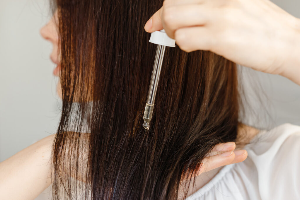 Hair care concept. Woman applying dropper with oil or serum essence on ends hair. Close up