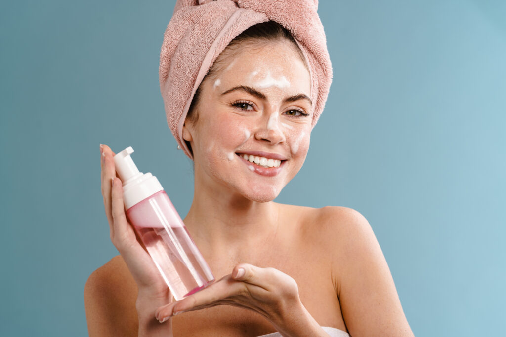 Shirtless happy girl using cleansing foam and smiling isolated over blue background. face wash cleanser