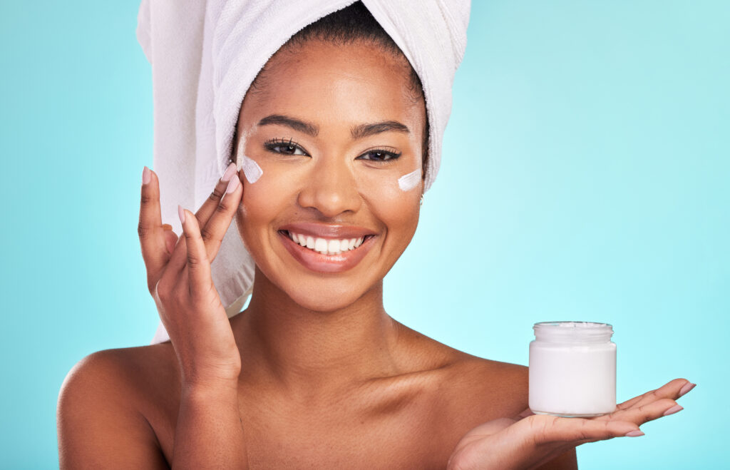 Skincare, beauty and portrait of black woman with cream, towel and smile in bathroom routine. face moisturizer 