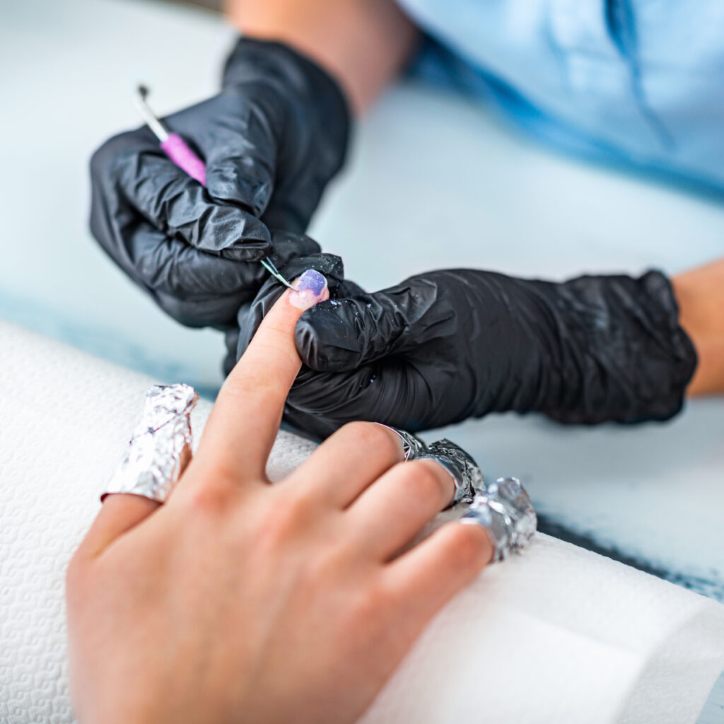 A faceless woman removing natural nail tips by soaking off her nails