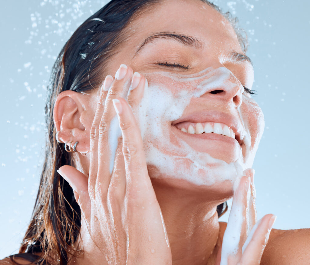 Studio shot of a young woman washing her face while taking a shower against a blue background. face wash cleanser